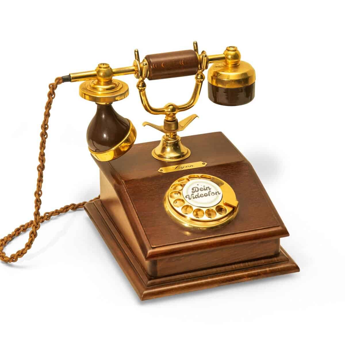 Ein altes Telefon mit Wählscheibe aus Holz und Gold, mit Hörer, Wählscheibe und Spiralkabel.